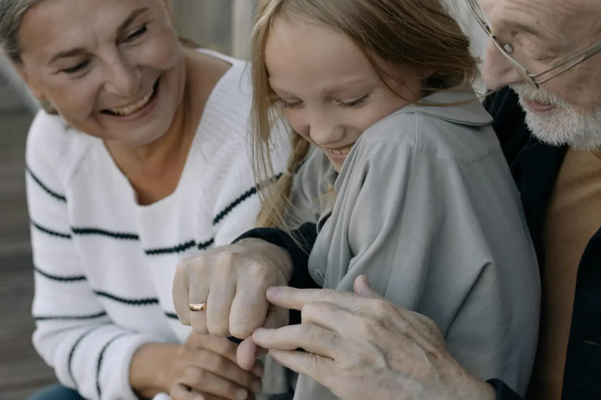 pexels-photo-7086012-7086012-1 Smiling grandparents sharing a joyful moment with their granddaughter outdoors.